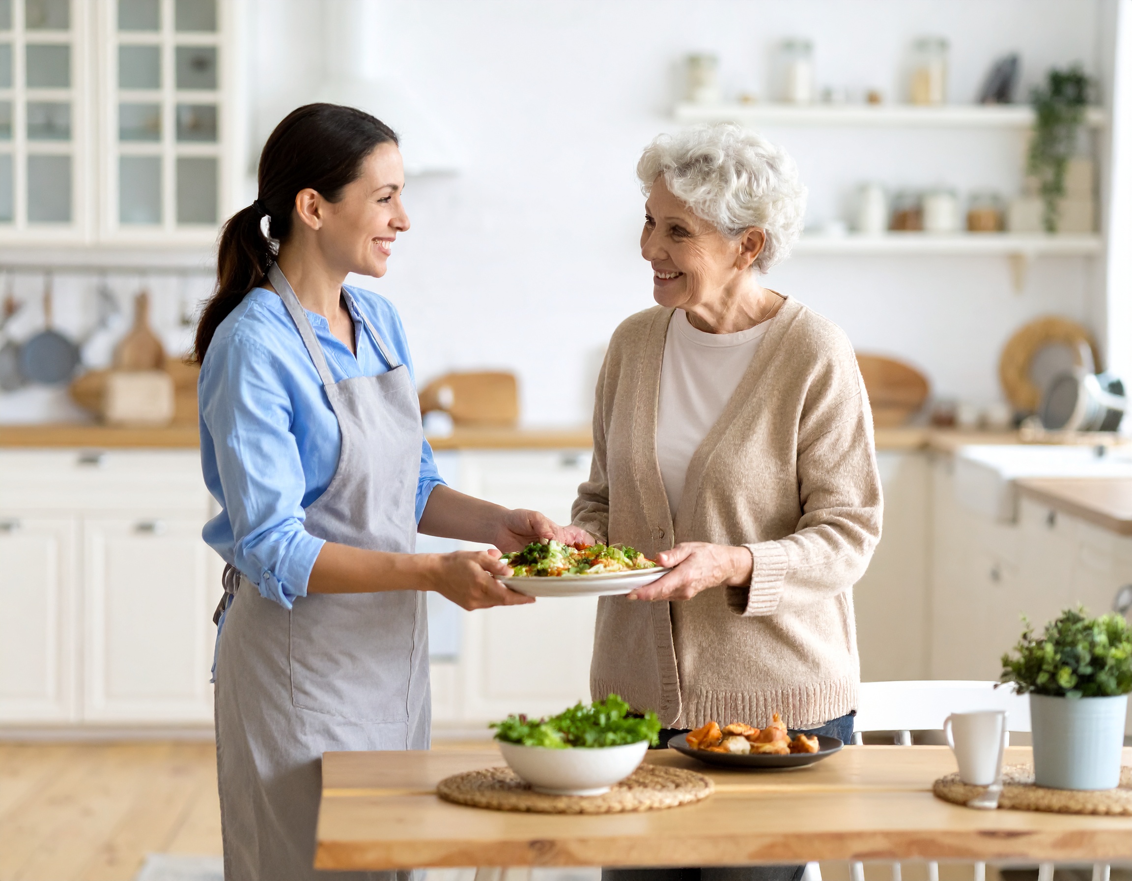 Pflegekraft unterstützt ältere Frau bei Haushaltsarbeiten und Essenszubereitung im gemütlichen Zuhause“</p>
<p>